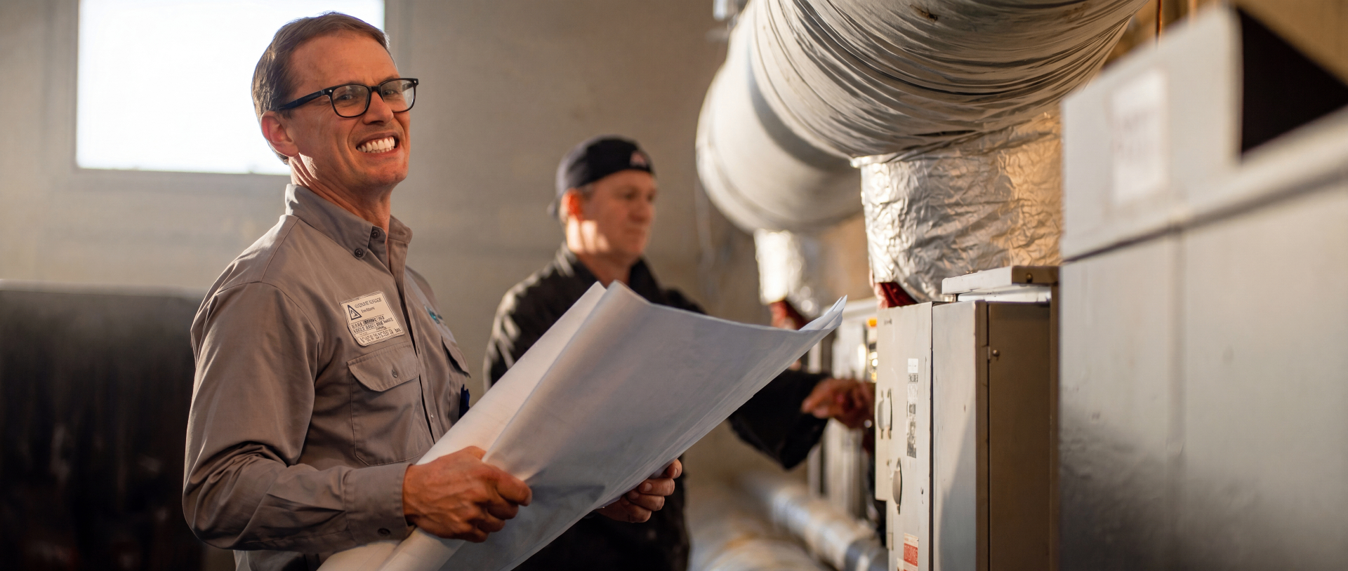 Industrial technicians reviewing blueprints alongside HVAC ductwork